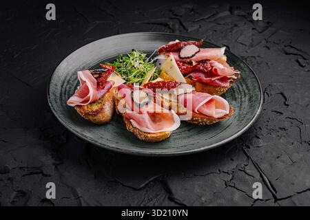 Köstliche Wurstplatte mit verschiedenen Aufschnitt- und Käsesorten, die elegant auf einem schwarzen Teller serviert werden Stockfoto