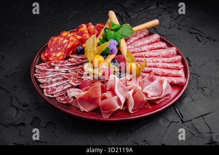 Räucherfleisch und Obst sind wunderschön auf einer dunklen Platte für eine Gourmet-Präsentation angeordnet Stockfoto