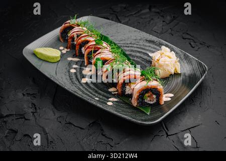Exquisite Sushi-Brötchen, die wunderschön auf einem modernen schwarzen Teller mit Verzierungen angeordnet sind Stockfoto
