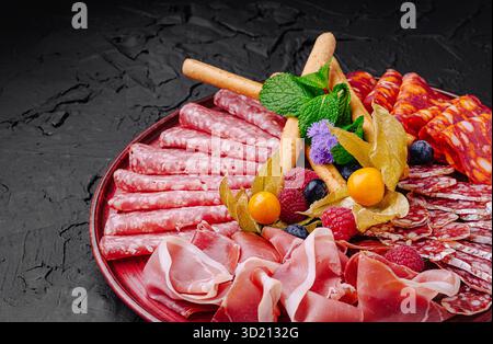 Räucherfleisch und Obst sind wunderschön auf einer dunklen Platte für eine Gourmet-Präsentation angeordnet Stockfoto