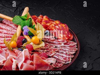 Räucherfleisch und Obst sind wunderschön auf einer dunklen Platte für eine Gourmet-Präsentation angeordnet Stockfoto