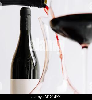 Eleganter Rotwein, der in eine Karaffe mit einem Glas daneben auf einem einfachen weißen Hintergrund gegossen wird Stockfoto
