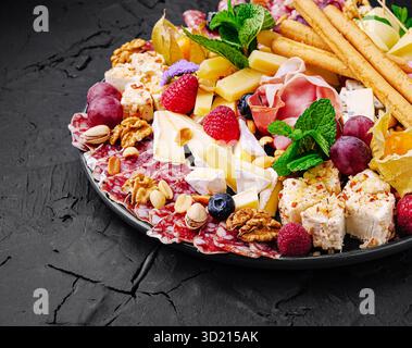 Exquisite Wurstplatte mit einer Auswahl an Käse, Aufschnitt, Früchten und Nüssen, die elegant für ein festliches Treffen präsentiert werden Stockfoto