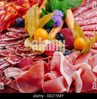 Räucherfleisch und Obst sind wunderschön auf einer dunklen Platte für eine Gourmet-Präsentation angeordnet Stockfoto