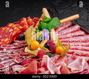 Räucherfleisch und Obst sind wunderschön auf einer dunklen Platte für eine Gourmet-Präsentation angeordnet Stockfoto