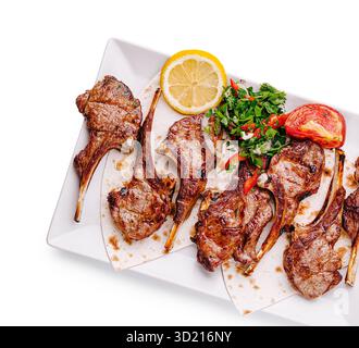 Gegrillte Lammkoteletts, serviert mit frischen Kräutern und Zitrone auf einem sauberen weißen Teller Stockfoto