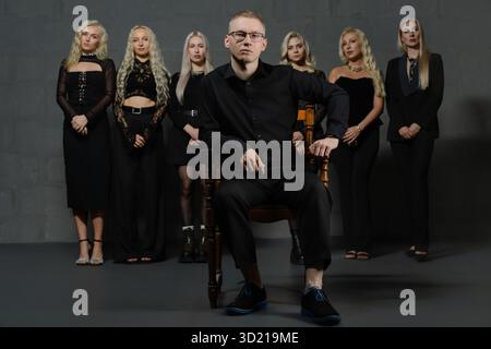 Gruppe von stilvollen Einzelpersonen, die in dramatischer Modeschaltung posieren, wobei einer vorne sitzt Stockfoto
