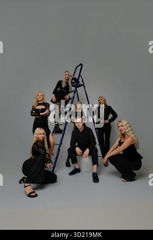 Eine Gruppe stilvoller Leute posiert kreativ um eine Leiter für ein Fotoshooting in einem Studio Stockfoto