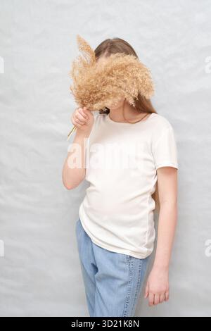 Kaukasische junge Frau im lässigen Outfit, die getrocknete Pampasgras gegen sie hält Stockfoto