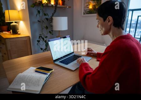 Reife Frau verfolgt Börsendiagramme und Kryptowährungskurse über App auf Laptop, Investitionen Stockfoto