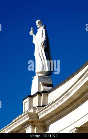 Weiße Statue des Heiligen mit Kreuz auf der Kirche vor blauem Himmel Stockfoto