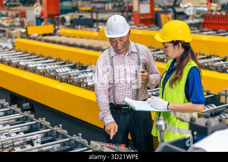 Arbeitnehmerinnen in einer Fabrik mit einer Schulung als leitender Vorgesetzter, die den Arbeitsauftrag in einer Metallblechfabrik überprüft Stockfoto