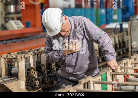 Brustschmerz eines leitenden Fabrikarbeiters, der an Herzinfarkt leidet, schwer arbeitendes Herzversagen, Zeichen-Ausdruck während des Arbeitsplatzes Stockfoto