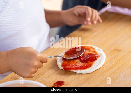 Kinder machen Mini-Pizza mit Tomatensauce Stockfoto