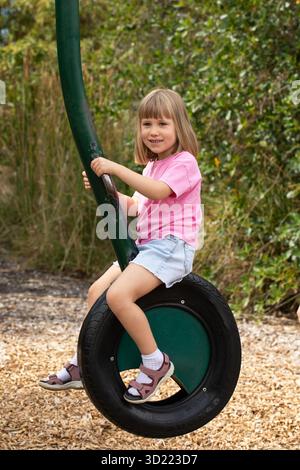 Ein süßes Mädchen spielt auf dem Spielplatz im Park. Ein fröhliches Kind auf einer Reifenschaukel im Park. Stockfoto