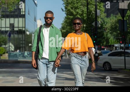 Fröhlich liebendes afroamerikanisches Paar lächelnd Spaziergänge in der Innenstadt zusammen Hände halten Genießen Sie den Spaziergang Stockfoto