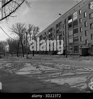 UdSSR, ukrainische SSR, 1960er Jahre Sloviansk, Oblast Donezk. Ein ruhiger Winterblick auf einen typischen Innenhof ('dvor') in einem neuen Wohnviertel, in der Nähe des zentralen Busbahnhofs. Ein langes, fünfstöckiges Wohnhaus aus Backstein (eine Chruschtschewka) dominiert die Szene. Dies war ein typisches Massengehäuse, das von der Armature and Isolator Plant (AIZ) für seine Arbeiter gebaut wurde. Der Hof und ein Kinderspielplatz (links) sind mit Schnee bedeckt und stark mit Fußabdrücken markiert. Dieses Schwarzweiß-Archivfoto fängt das tägliche Leben einer sowjetischen Stadt ein. Stockfoto