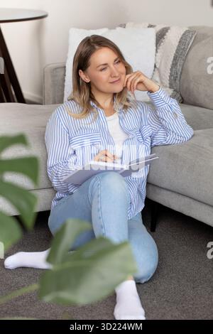 Die Frau schreibt interessante Gedanken im Tagebuch, die auf dem Boden sitzt Stockfoto