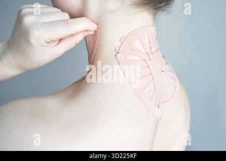 Weibliche Anwendung von therapeutischem Klebeband am oberen Rücken zur Schmerzlinderung und Haltung Stockfoto