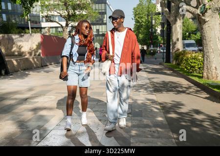 Fröhliches afroamerikanisches Liebespaar, das in der Stadt spaziert, bringt Freundin zum Lachen. Stockfoto