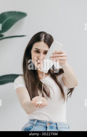 Happy Woman gießt Shampoo in die Handfläche aus einer Plastikflasche im Lichtstudio Stockfoto