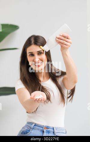 Happy Woman gießt Shampoo in die Handfläche aus einer Plastikflasche im Lichtstudio Stockfoto