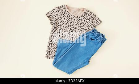 Ein Set stilvoller Kleidung für Kinder. Jeans und ein T-Shirt auf beigefarbenem Hintergrund für ein Mädchen. Stockfoto