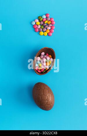 Schokoladen-Osterei mit bunten Dragees innen auf einem Blau. Frohe Ostern. Stockfoto