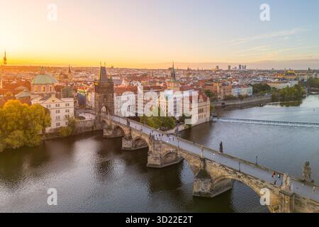 Die Morgensonne beleuchtet die Prager Burg sanft im Hintergrund, während die Menschen über die Karlsbrücke über die Moldau schlendern und eine ruhige Frühtagsszene in Prag schaffen. Stockfoto