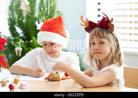 Niedliche Brüder und Schwester in Weihnachtskostümen schreiben einen Brief an den Weihnachtsmann. Silvester Stockfoto