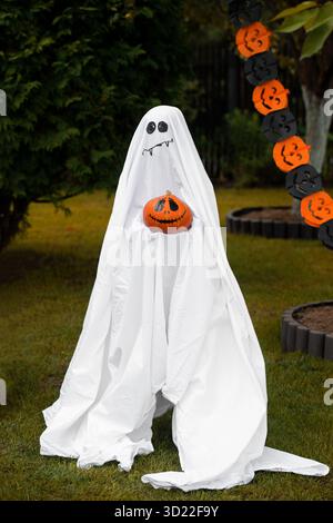 Person im Geisterkostüm mit gruseligen Kürbissen im Hinterhof Stockfoto