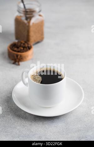 Schwarzer Kaffee in einem weißen Becher auf einer Untertasse auf einem grauen Tisch. Sofortiger Kaffee. Stockfoto