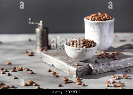 Geröstete Kaffeebohnen in einer Schüssel auf einem grauen Brett und Kaffeemühle auf dunklem Hintergrund. Stockfoto
