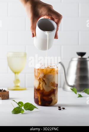 Die Creme wird in kalten schwarzen Kaffee mit Eiswürfeln gegossen. Coldbrew. Sommergetränke. Stockfoto