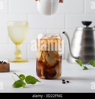 Die Creme wird in kalten schwarzen Kaffee mit Eiswürfeln gegossen. Coldbrew. Sommergetränke. Stockfoto