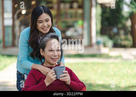 Asiatische Seniorin im Rollstuhl mit glücklicher Tochter. Familie Beziehung Rentnerin sitzend auf Rollstuhl im Park Alter ca. Stockfoto