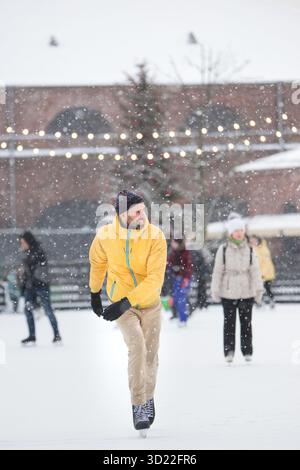 Fröhlicher Mann mittleren Alters in gelber Jacke, beigefarbene Hosen auf der Eisbahn, draußen an schneebedeckten Wintertagen Stockfoto
