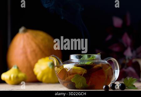 Herbsttee mit Zitrone, Gewürzen und Johannisbeerbeeren in einer Teekane auf dem Hintergrund von Kürbissen und Kürbis. Herbststimmung. Stockfoto