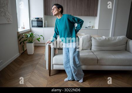 Reife Frau in Qualen, die zu Hause unter Rückenschmerzen leidet. Eingeschränkte Mobilität, körperliche Schwierigkeiten Stockfoto