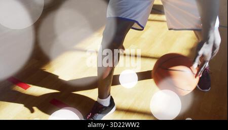 Tribbelnder männlicher Athlet in weißen Shorts, schwarzen Schuhen auf dem Hartholzplatz, mit orangefarbenem Basketball Stockfoto