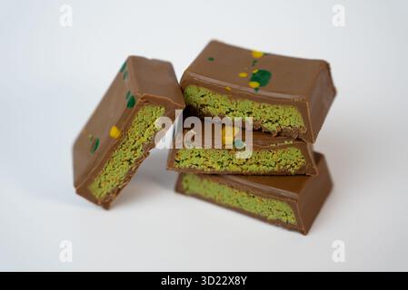 Stapel Schokoladentafeln gefüllt mit Pistaziencreme auf weißem Hintergrund. Elegantes Gourmet-Dessertkonzept für Café-, Verpackungs- oder Konditormarken. Stockfoto
