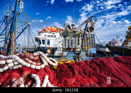 Ein farbenfrohes Fischerboot legt an einem Hafen an, umgeben von leuchtenden roten und weißen Netzen. Essaouira, Marokko Stockfoto