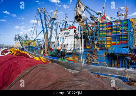 Farbenfrohe Fischerboote legen an einem belebten Hafen unter einem hellblauen Himmel mit verstreuten Wolken an. Essaouira, Marokko Stockfoto