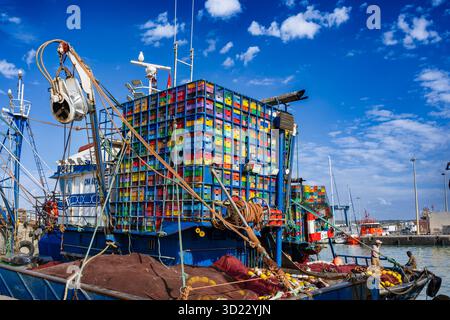 Fischerboote mit bunten Kisten an einem geschäftigen Hafen unter klarem blauen Himmel. Essaouira, Marokko Stockfoto