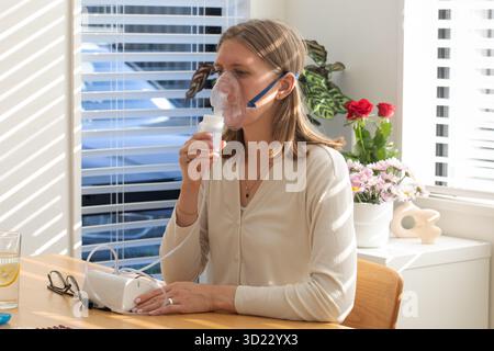 Frau, die Vernebler für Atemgesundheit in einem hellen Zuhause verwendet. Gesundheitsbegriff Stockfoto