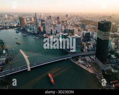 Blick aus der Vogelperspektive auf eine geschäftige Stadtlandschaft mit einer Hängebrücke über einen Fluss bei Sonnenuntergang. Ho-Chi-Minh-Stadt, Vietnam Stockfoto