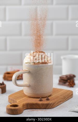 Kakaopulver auf Schlagsahne in der Tasse auf dem Schneidebrett gießen Stockfoto