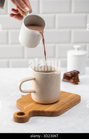 Kakao aus einer kleinen Kanne auf dem Tisch in einen Keramikbecher gießen Stockfoto
