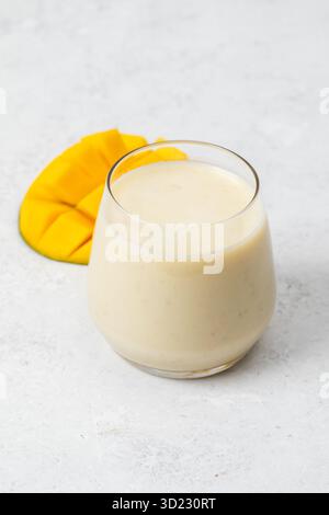 Erfrischender Mango-Smoothie in einem Glas mit geschnittener Mango auf hellem Hintergrund Stockfoto