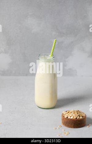 Erfrischender Hafermilch-Smoothie mit Strohhalm in Glasflasche auf grauer Oberfläche. Entgiftung Stockfoto